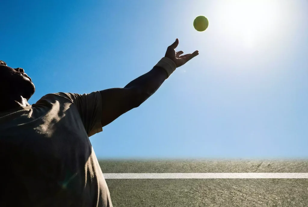 Tenista lanzando la pelota al aire en el momento del saque con el cielo de fondo