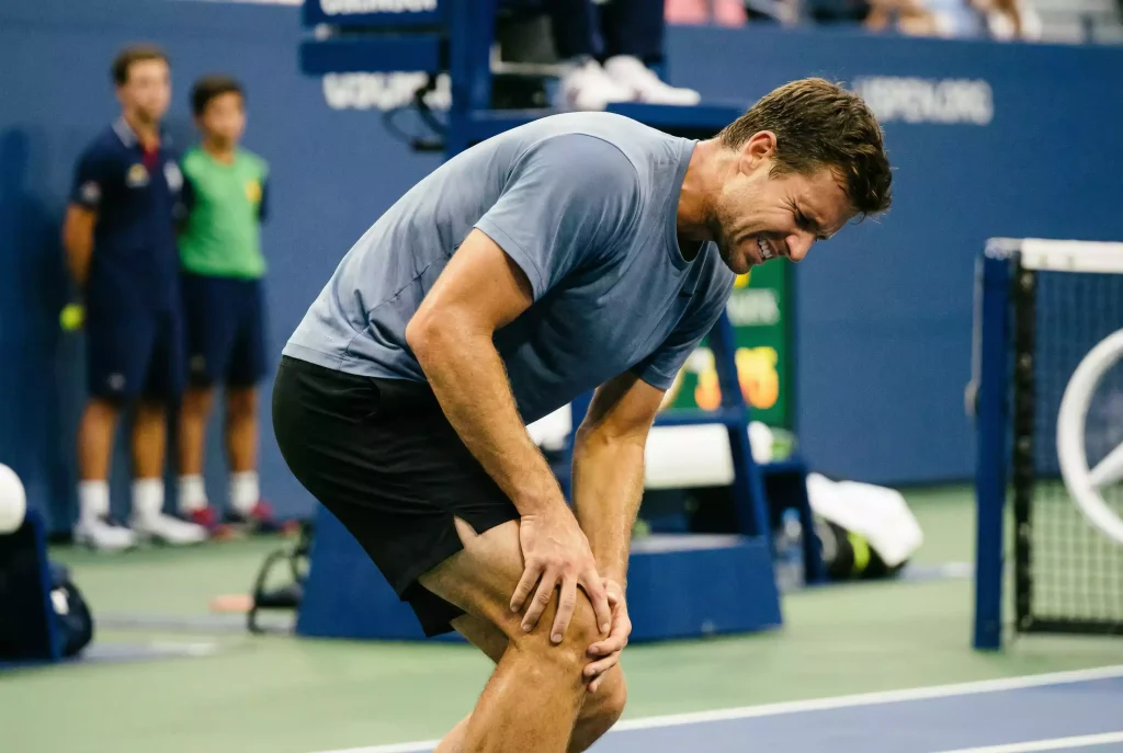 Tenista tocándose la rodilla con gesto de dolor durante un partido de tenis
