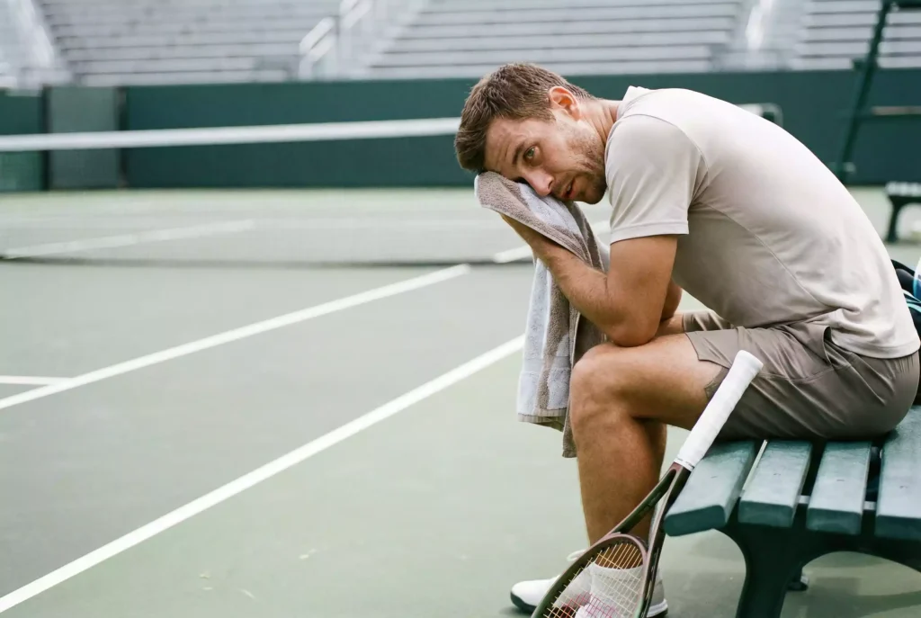 Tenista sentado en la silla durante un cambio de lado secándose el sudor con una toalla