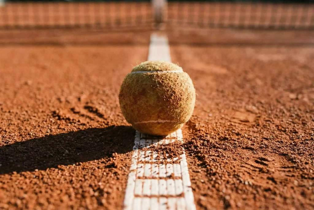 Primer plano de una pelota de tenis sobre la línea blanca de una pista de tierra batida